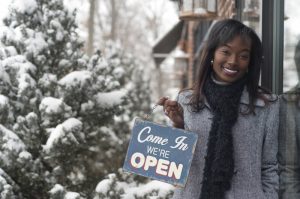 black-woman-business-owner-stands-outside-shop-holding-open-sign-in-winter